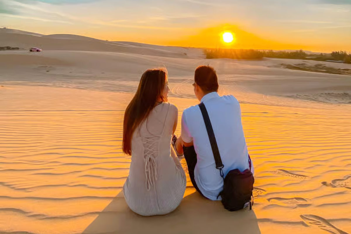 Couple watching sunset over Red Sand Dunes in Mui Ne, with golden sky and red sand landscape
